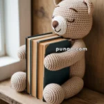A crocheted teddy bear holding a stack of hardcover books, sitting on a wooden shelf by a window.