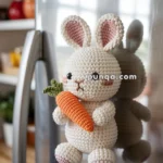 A crocheted bunny magnet with pink ears and a carrot, attached to a stainless steel refrigerator door in a kitchen setting.