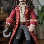 A crochet doll resembling a pirate with a red coat detailed with gold embroidery, a feathered tricorn hat, a hooked hand, and black boots, standing on a wooden box.