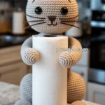 A crocheted cat-shaped paper towel holder with a roll of paper towels, set on a kitchen countertop.