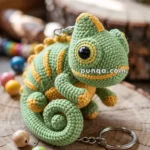 A crocheted chameleon keychain with green and yellow yarn sits on a wooden surface, surrounded by colorful beads.