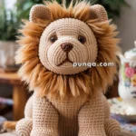 A hand-crocheted lion toy with a fluffy mane sits on a wooden table, surrounded by indoor plants.