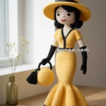 A crochet doll wearing a yellow dress with black trim, a matching wide-brimmed hat, and holding a round yellow handbag with black tassels, is displayed on a wooden table near a window, with a vase and a notebook beside it.