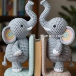 Two crocheted elephant bookends in gray with colorful ear accents holding a book upright on a wooden surface in a cozy room setting.