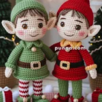 Two crocheted elf dolls with large ears and Christmas-themed outfits, one in green with red and white striped leggings, and the other in red with green shoes, standing on a pink braided mat surrounded by white pom-poms and small gift boxes.