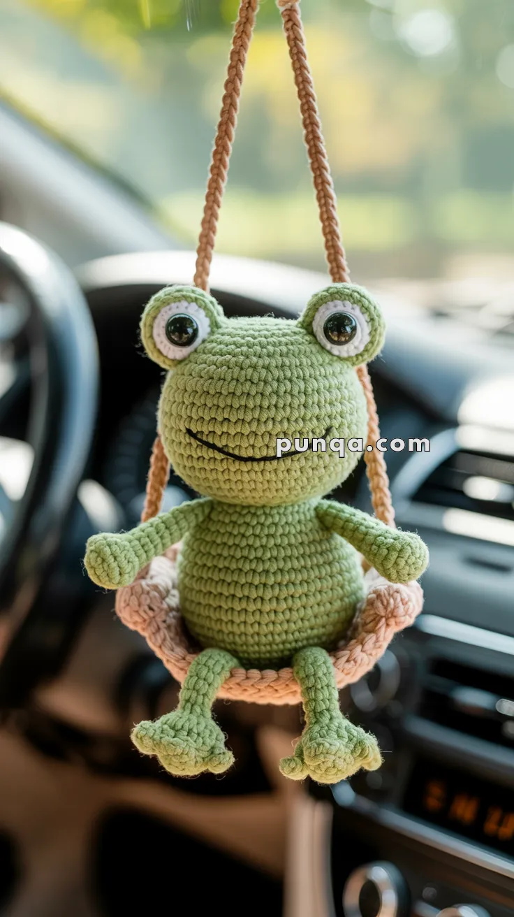 A crocheted green frog hanging from a string inside a car, with the dashboard visible in the background.