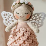 A crocheted angel doll with a floral headband, pink scalloped dress, and white wings, hanging by a ribbon.