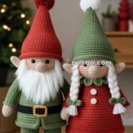 Two crochet gnomes stand side by side; one wearing a red hat and green outfit with a white beard, and the other in a green hat and red dress with white braids.