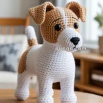 A handmade crocheted dog toy with brown and white patches, standing on a wooden table in a cozy room.
