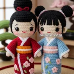 Two crocheted dolls in traditional Japanese kimonos, one red and one blue, with floral patterns, standing on a woven mat in a room with sliding shoji doors.