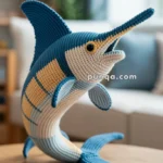 A crocheted marlin fish in blue and beige colors displayed on a wooden table, with a blurred living room background.