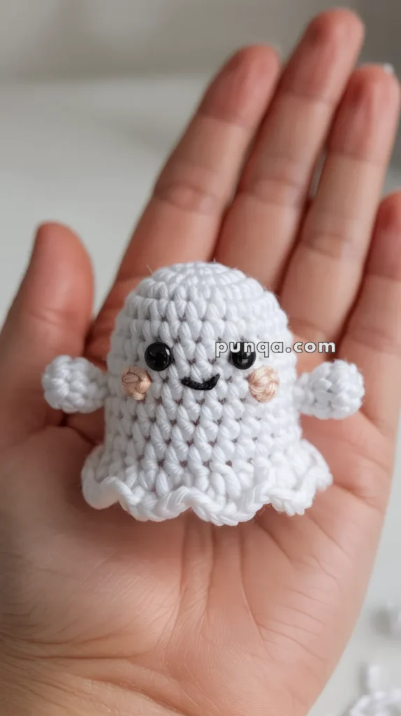 A small crocheted ghost with a cute smiley face and pink cheeks, held in the palm of a hand.