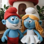 Crocheted Papa Smurf and Smurfette characters with a mushroom-shaped house in the background; one wears a red hat and pants, the other has long yellow hair and a white dress.