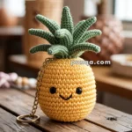 A cute crocheted pineapple keychain with a smiling face, sitting on a wooden surface, surrounded by a softly blurred indoor setting.