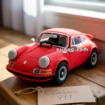 A crochet model of a classic red 911 sports car placed on a wooden table beside a label reading "Classic 911" in a sunlit room.