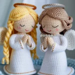 Two crocheted angel figures with white robes and golden accents, featuring wings and halos, are positioned side by side on a textured blue surface.