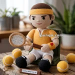 Crocheted doll dressed as a tennis player wearing a yellow outfit and headband, holding a crocheted tennis racket, surrounded by crocheted tennis balls on a wooden table labeled 'Champion.'