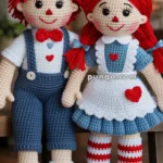 Two handmade crocheted dolls wearing matching outfits, with one doll in blue overalls and a white shirt, and the other in a blue dress with a white apron. Both have red yarn hair and are decorated with red hearts.