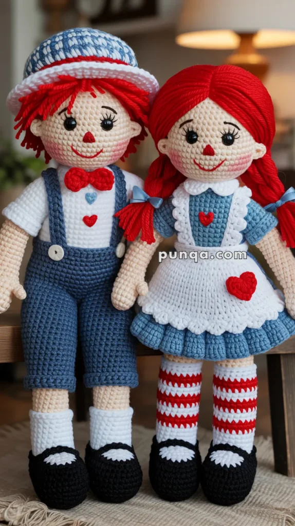 Two handmade crocheted dolls wearing matching outfits, with one doll in blue overalls and a white shirt, and the other in a blue dress with a white apron. Both have red yarn hair and are decorated with red hearts.
