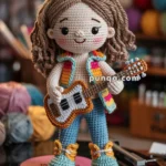 A crocheted doll with long brown hair, wearing a colorful vest and blue pants, holding a small guitar, and standing on a vinyl record in a craft room.