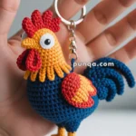 Close-up of a hand holding a colorful crocheted rooster keychain with red, yellow, and blue yarn details.