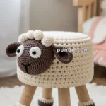 A knitted ottoman shaped like a sheep, with a woolen texture covering and wooden legs, placed on a fluffy white rug in a cozy room setting.
