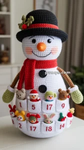 A crocheted snowman with a black hat, red scarf, and colorful mini plush toys in numbered pockets on its body, functioning like an advent calendar.