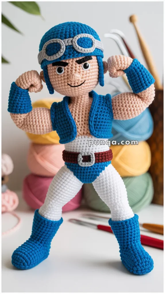 A crocheted doll wearing a blue helmet, goggles, and a sleeveless blue vest, with white pants and blue boots, standing in front of a background with pastel yarn balls and crochet hooks.