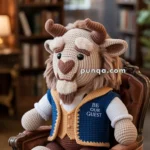 A crocheted plush toy resembling a beast with horns, sitting in an armchair, dressed in a blue vest with the words 'BE OUR GUEST' embroidered on it, in a room lined with bookshelves.