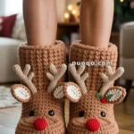 Person wearing knit reindeer slippers with red noses and antlers, standing on a wooden floor.