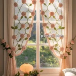 A cozy bedroom scene with crochet curtains decorated with pink crochet roses in front of a sunlit window. The window overlooks lush greenery outside. Below the window is a small white table with a soft-glowing lamp and a bouquet of pink roses, with the word "Amor" inscribed on the table. A portion of a bed with white bedding is visible in the foreground.