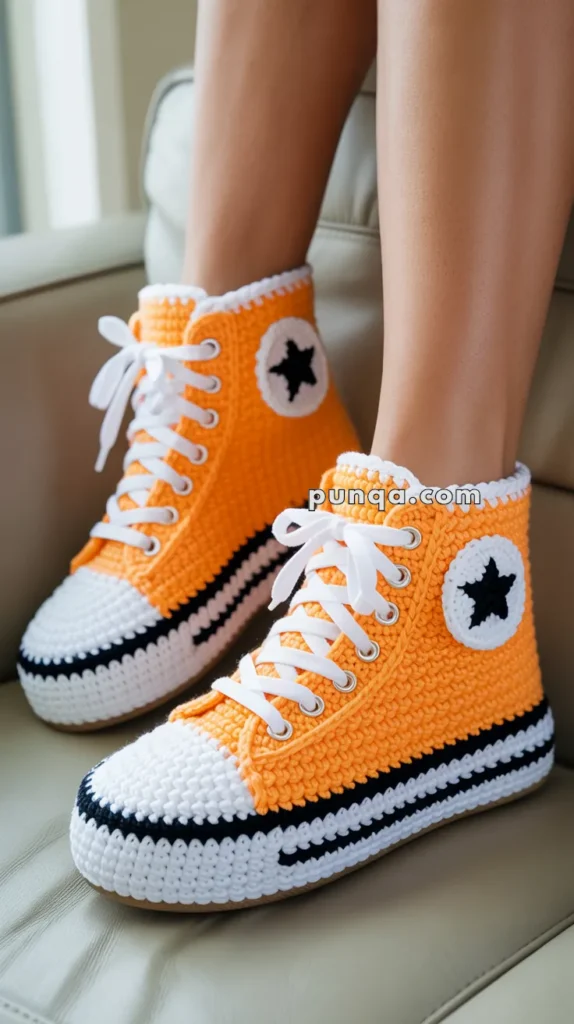 A pair of orange crochet sneakers with white laces and black star patterns, worn by a person sitting on a beige couch.