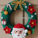 A crocheted Christmas wreath featuring a Santa Claus face, red flowers, and festive decorations like a candy cane and gift ornaments, adorned with a gold rope bow, hanging on a door.