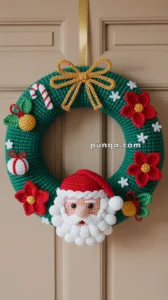 A crocheted Christmas wreath featuring a Santa Claus face, red flowers, and festive decorations like a candy cane and gift ornaments, adorned with a gold rope bow, hanging on a door.