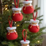 Crocheted red and white pom-pom decorations shaped like sacks, hanging from a Christmas tree branch.