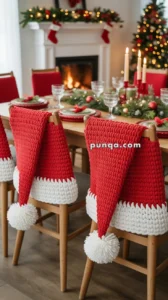 A festive dining room with chairs covered in red and white knitted Santa hat chair covers, a decorated Christmas tree, a fireplace with stockings, and a table set for a holiday meal with candles and greenery.